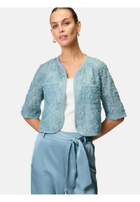 Helles blaues cropped Jackett mit floraler Textur, kurzen Ärmeln und zwei vorderen Taschen, kombiniert mit hellblauen, schmal geschnittenen Hose mit Schleife.