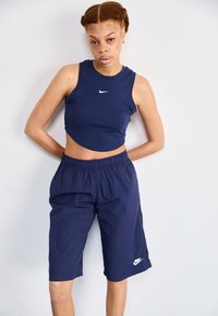 Tamna plava uska majica bez rukava s bijelim Nike logotipom, u kombinaciji s tamnoplavim hlačama do koljena s elastičnom trakom u struku i akcentima logotipa.
