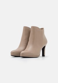 Stivaletti in pelle beige alla caviglia con punta appuntita, colletto scallop e tacco alto sottile. Texture liscia, design minimalista e senza decorazioni.
