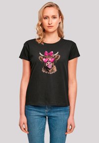 Black short-sleeve t-shirt featuring a graphic of a cartoon cow with pink sunglasses and a bow, printed on a soft, casual fabric.
