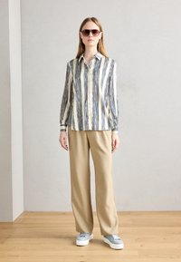 Knappe skjorte med vertikale blå og hvite striper, kombinert med beige vide bukser og grå platå sneakers. Solbriller inkludert.
