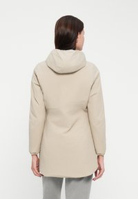 Beige gewatteerde jas met een matte afwerking, elastische boorden en een aangesnoerde taille. Lichtgewicht, met een gladde textuur en lange mouwen.