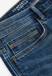 Denim jeans met een "Comfort Stretch" label. Donkerblauwe stof met een vervaagde afwerking, verticale stiksels en een klein voorvak.