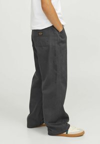 Sive široke hlače iz trdnega bombaža, ki imajo stranske žepe, zadnji žepek in kontrastne šive. Oblečene z belo srajco.