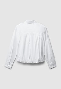 Chemise blanche à manches longues avec des poignets boutonnés et un ourlet froncé, vue de dos sur un fond gris clair uni.
