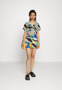 Conjunto de duas peças com padrão abstracto colorido, incluindo um top cropped com cordão, calções a condizer e sandálias abertas pretas.