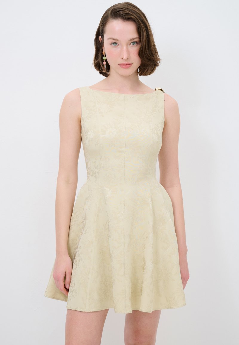 Romantische crèmekleurige jurk met bloemenpatroon, een getailleerde bodice, een uitlopende rok en een schouderdetail. Gemaakt van textuurstof, met een subtiele glans.