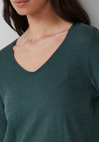 Top in cotone leggero e verde scuro a scollo a v, con una finitura testurizzata e maniche corte, che presenta una vestibilità comoda e dettagli di design discreti.