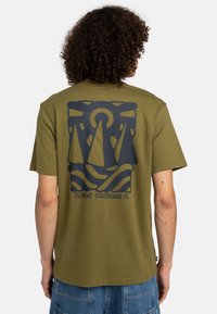 T-shirt en coton olive avec un graphique bleu foncé représentant deux formes triangulaires, des vagues et le texte "ELEMENT SKATEBOARD CO." Manches courtes.