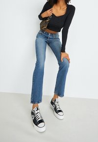 Top negro de manga larga, jeans acampanados azules y zapatillas negras y blancas. Tejido texturizado, diseño corto y detalle de cintura alta.