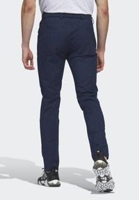 Marineblauwe broek met een slim fit, gemaakt van een gestructureerde stof en voorzien van twee achterzakken. Draagt een paar zwart-witte sneakers met een patroon.