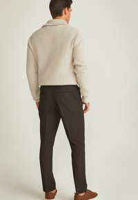 Beige geribde trui met een sjawlboord, gecombineerd met donkere taps toelopende broeken. Bruine schoenen maken de outfit compleet, gezien vanuit de achterkant.