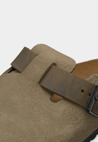 Κοντινό πλάνο μπεζ σουέντ κλογκ με φαρδιά καφέ δερμάτινη λουρίδα και ασημένια αγκράφα.