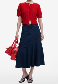 Punainen lyhyt neule, farkkuhame epäsymmetrisellä helmalla, siniset avokkaat ja punainen käsilaukku hitsatuilla kahvoilla.