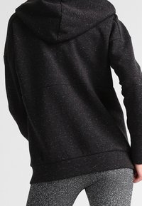Sweat à capuche noir avec un tricot texturé, doté d'une coupe ample et d'une poche kangourou. Le tissu présente un motif tacheté subtil.