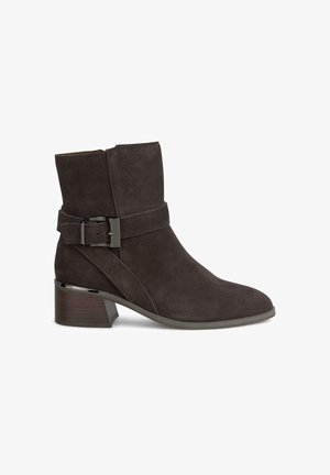 Botín de ante gris oscuro con puntera redondeada, correa envuelta con una hebilla de plata y un tacón bajo apilado. Textura suave.