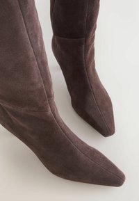 Brown suede knee-high boots with a pointed toe and smooth texture, featuring a side zipper and angled seams for a fitted design.