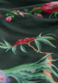 Ein blumendekorierter Stoff hat eine dunkelgrüne Basis mit pink- und roten Blumen, grünen Blättern und feiner Netzstruktur.