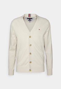 Cárdigan crema con escote en V y cinco botones dorados. Presenta un detalle a rayas en azul marino y rojo en el cuello y puños acanalados.