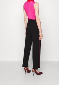 Strak zittend, mouwloos roze topje met geribbelde textuur, gecombineerd met losse zwarte broek met een zijstreep en bordeauxrode hoge hakken.