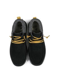 Black suede shoes with gray felt lining, featuring yellow laces and rubber soles. Rounded shape with decorative stitching detail.