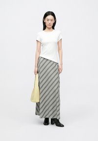 Hvid tætsiddende T-shirt kombineret med en gråstribet maxi-nederdel. Modellen holder en gul taske og har sorte støvler med hæl på. Neutral baggrund.