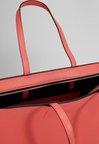 Sac cabas corail en similicuir lisse et texturé, accents noirs, deux poignées plates, fermeture éclair et intérieur spacieux doublé de tissu noir.