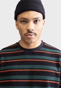 Gorro negro; suéter de rayas en verde oscuro, negro y naranja; tejido texturizado; cuello acanalado; rayas horizontales de anchos variables.