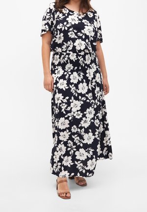 Maxikleid mit floralem Muster auf navyblauem Hintergrund, großen cremefarbenen Blumen, kurzen Ärmeln und einem gerafften Taillenbereich. Kombiniert mit sandfarbenen Sandalen.