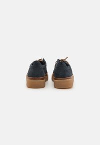 Sneakers de camurça azul-marinho com uma sola de borracha castanha, bico redondo, design de cadarço e detalhes costurados nas laterais e no calcanhar.