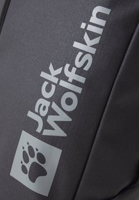 Sivý batoh s hladkým, odolným materiálom. Obsahuje branding 'Jack Wolfskin' a logo stopy labky, oboje v svetlosivej farbe.