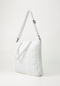 Sac fourre-tout blanc matelassé avec un extérieur rembourré, une sangle réglable et une poignée supérieure. Présente des motifs rectangulaires sur la surface.