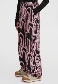 Zwarte broek met wijde pijpen met een roze en witte abstracte print, voorzien van zijzakken en een gestructureerde stof, gecombineerd met beige en bruine schoenen.