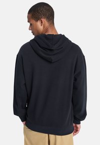 Sudadera con capucha de color navy hecha de tela suave, con un corte relajado, hombros caídos y puños y dobladillo de canalé para mayor comodidad.