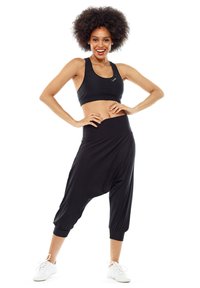 Sujetador deportivo negro combinado con pantalones tipo harem negros. Los pantalones tienen un corte ajustado en los tobillos y una cinturilla ancha y elástica.