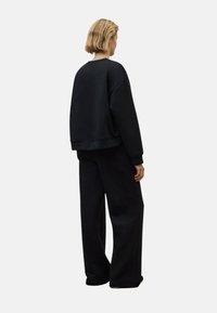 Sudadera negra de gran tamaño y pantalones de pierna ancha en una tela suave y texturizada; diseño sencillo con puños y cintura acanalados.