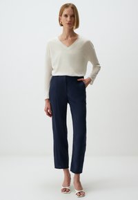 Witte V-halstrui gecombineerd met marineblauwe op maat gemaakte broeken. De outfit heeft strakke lijnen, een relaxed fit en casual witte open-toe hakken.