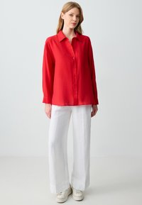 Red, long-sleeve button-up shirt in lightweight fabric, paired with white wide-leg linen pants and white sneakers.