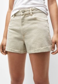 Shorts in denim beige con orlo sfrangiato, vita alta e tasche frontali. Il tessuto ha una leggera trama, progettati per un abbigliamento informale.