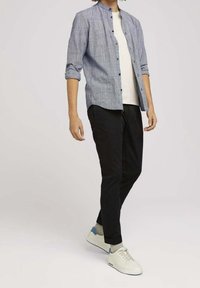 Camisa de cuadros azul sobre una camiseta blanca, combinada con pantalones negros y zapatillas blancas con detalles azules.