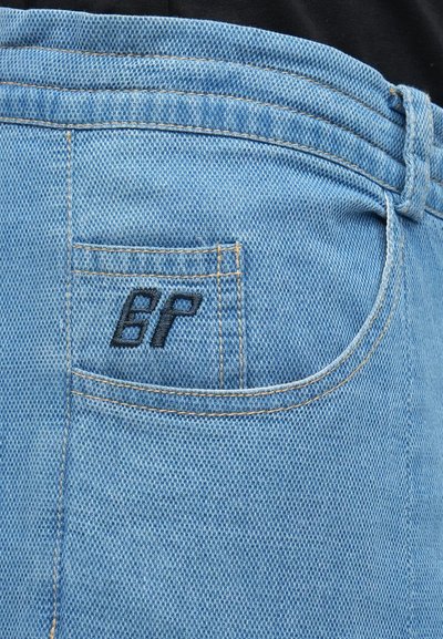 Κοντινό πλάνο τσέπης από ανοιχτό μπλε τζιν με μικρά μαύρα κεντημένα γράμματα "BP" και εμφανείς ραφές.