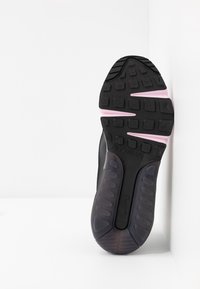 Semelle d'une basket noire et rose avec semelle texturée, coussin d'air et logo Nike visible sur fond blanc.