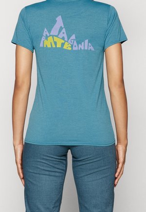 Person iført en blå t-shirt med en bjergformet grafik og ordene "Patagonia MTB" i lilla og gul på ryggen.