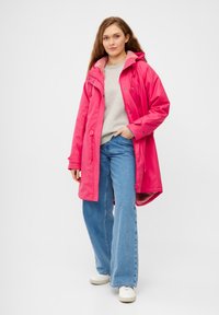 Ljust rosa vattentålig jacka med mjukt innerfoder, utrustad med huva, justerbara dragskor och tryckknappsstängning, som bärs över ljus denim.