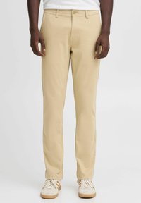 Beige cotton chinos with a straight leg design, featuring a front button closure and belt loops, paired with light-colored sneakers.