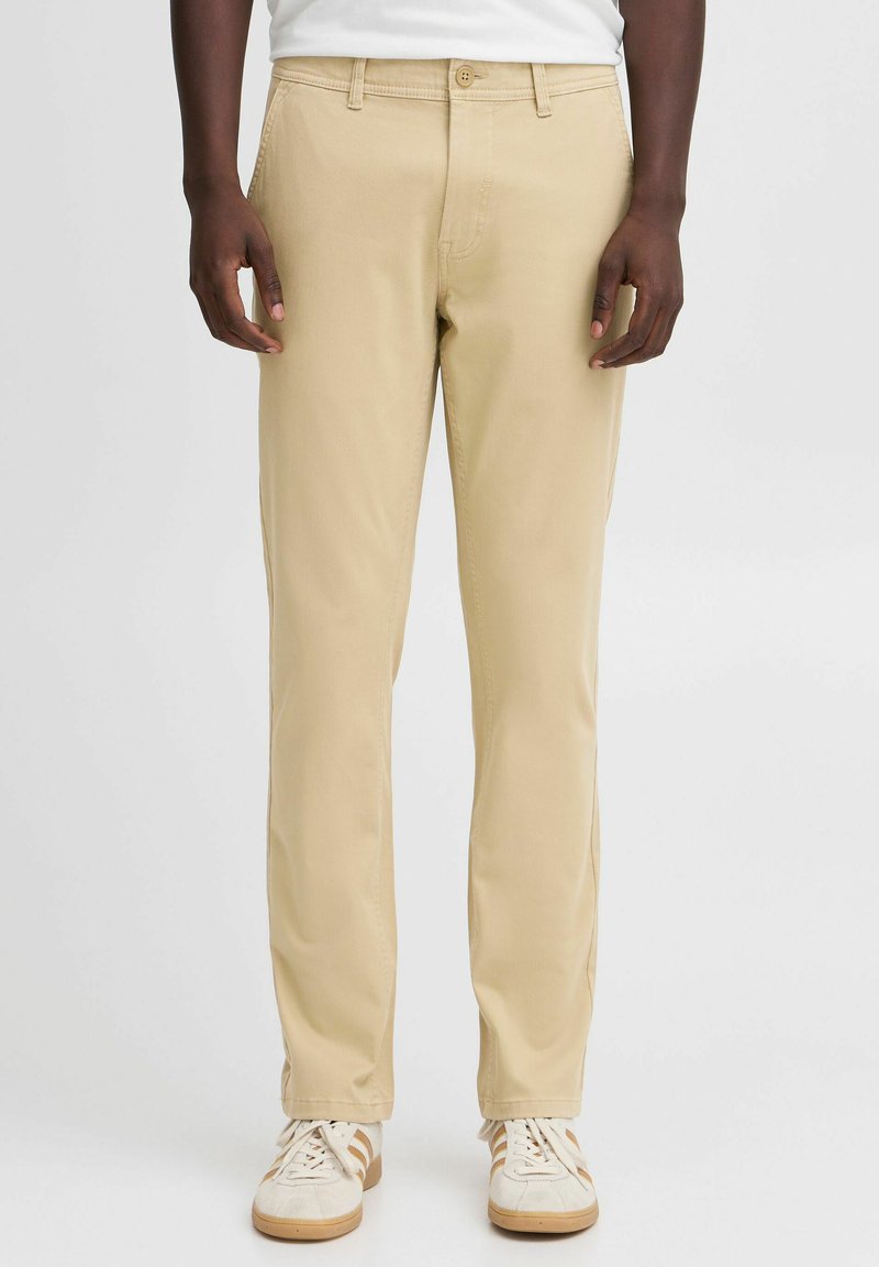 Beige cotton chinos with a straight leg design, featuring a front button closure and belt loops, paired with light-colored sneakers.