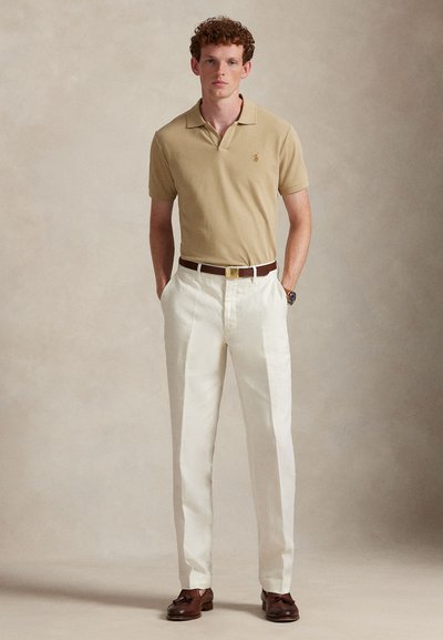 Μπεζ πόλο πουκάμισο με γιακά, λευκό λινό παντελόνι, καφέ ζώνη και καφέ παπούτσια. Κλασική εφαρμογή με διακριτική λεπτομέρεια λογότυπου στο πουκάμισο.