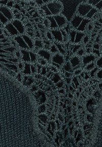 Fil foncé avec une dentelle au crochet détaillée présentant des motifs circulaires et floraux à côté d'une section de tissu tricoté serré.