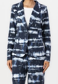 Blazer bleu marine avec un motif abstrait blanc et bleu. Il présente un col cranté, deux poches avant et une fermeture à un seul bouton.