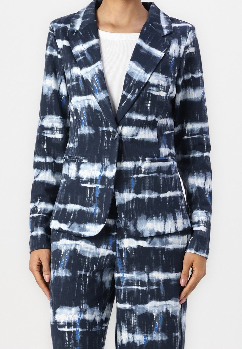 Blazer bleu marine avec un motif abstrait blanc et bleu. Il présente un col cranté, deux poches avant et une fermeture à un seul bouton.